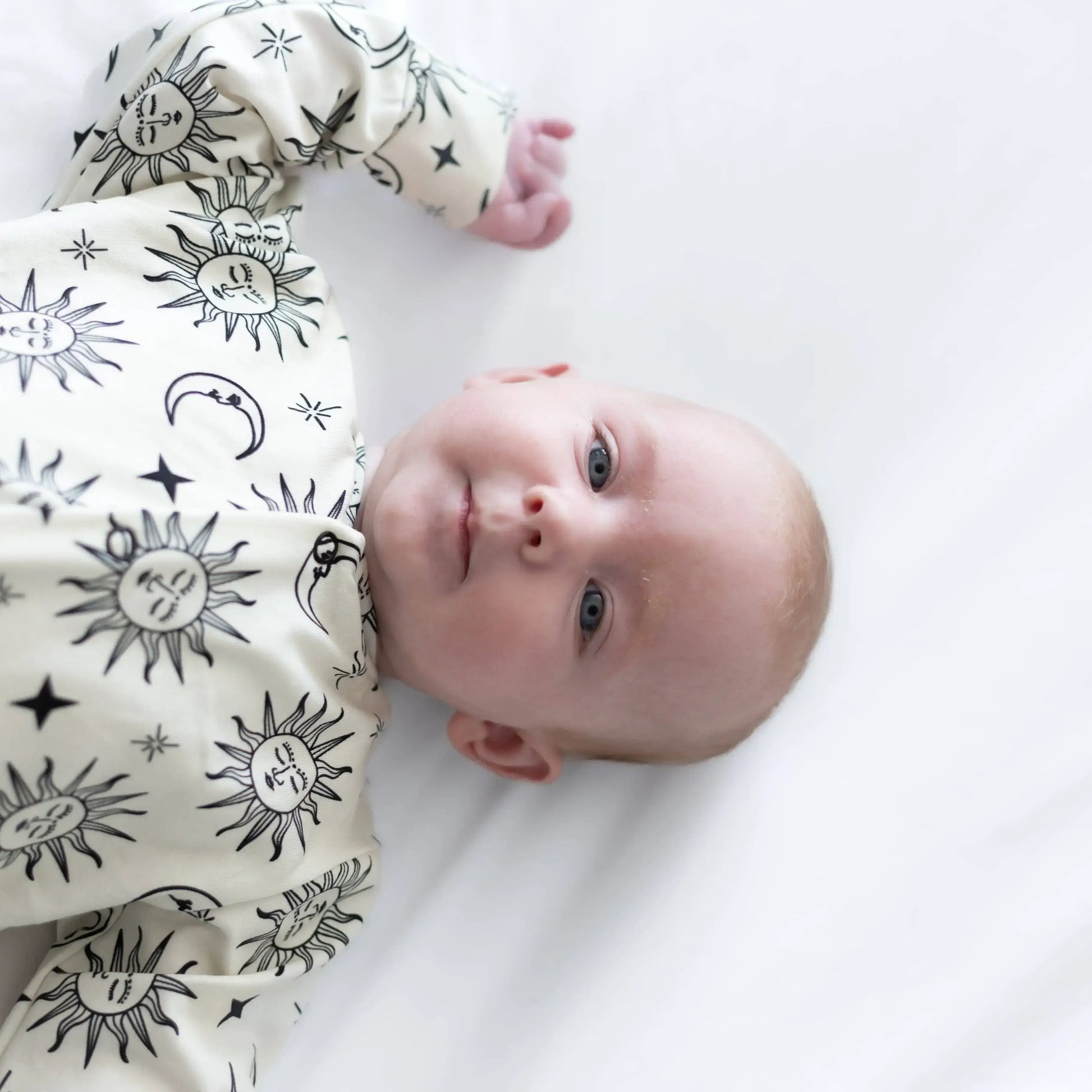 Baby wearing a sleepsuit with black sun and moon patterns on a white background