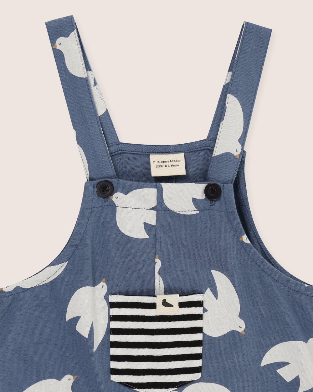 Blue dungaree with white bird pattern and black and white striped pocket on a light gray background