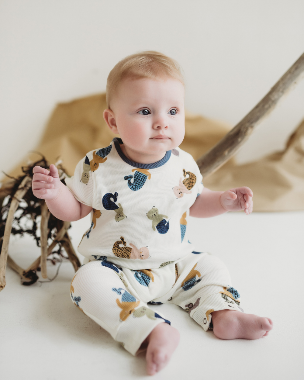 Baby wearing a sleepsuit with animal prints sitting on a white surface.