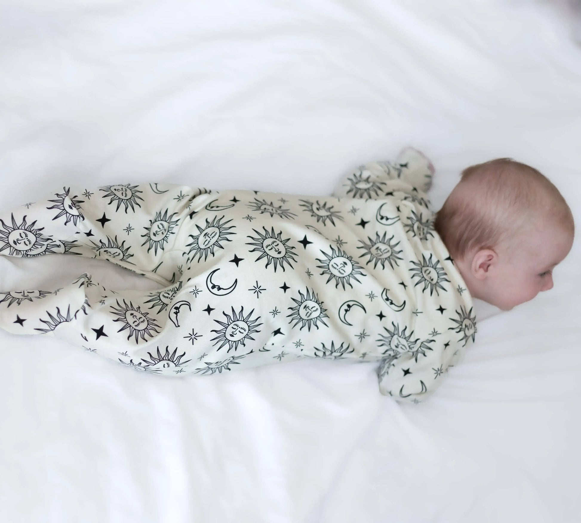 Baby wearing sleepsuit with celestial pattern on a white surface