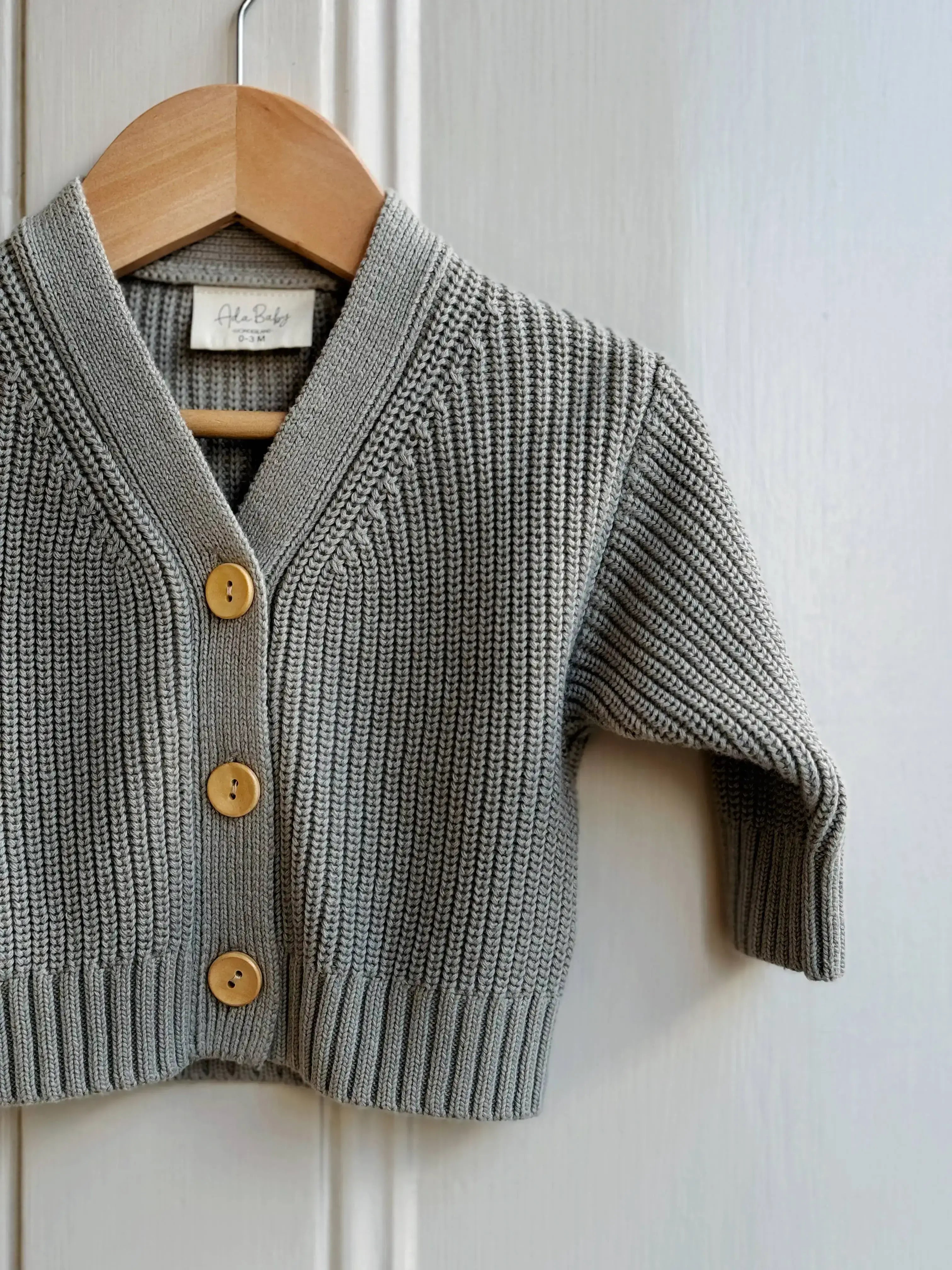 Light green knitted cardigan with wooden buttons on a hanger against a white background