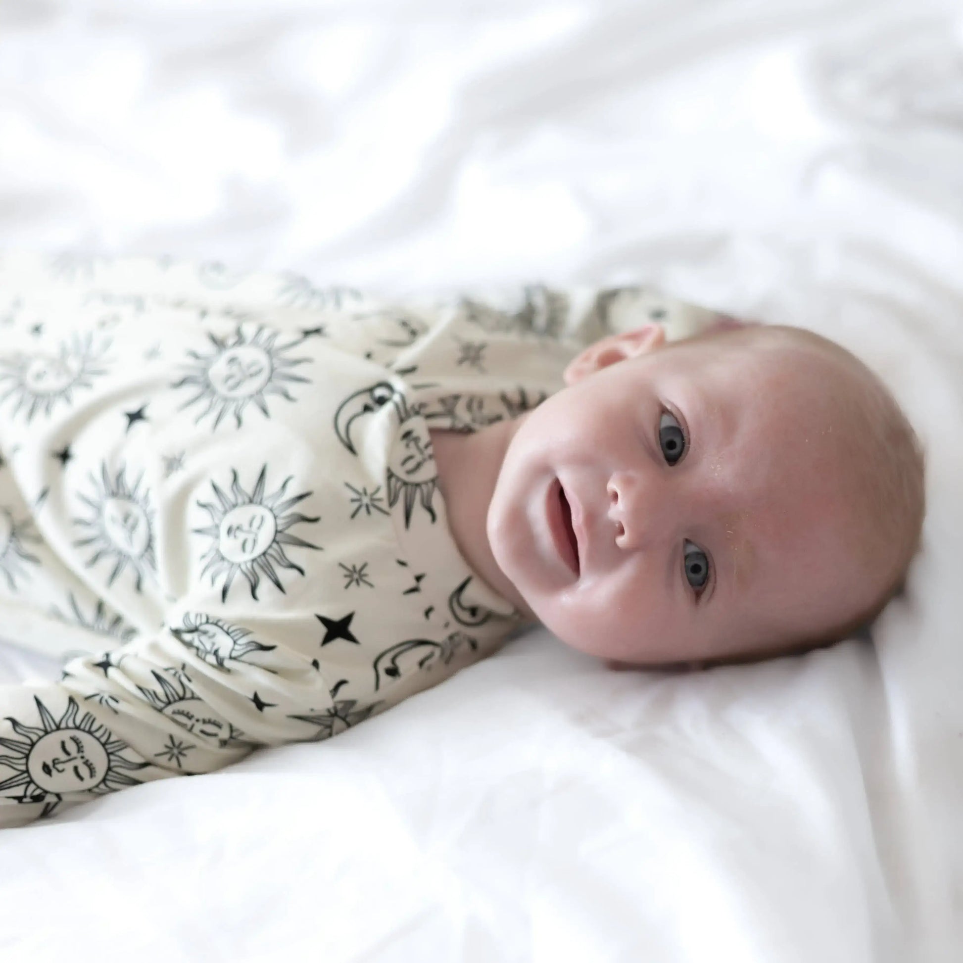 Newborn baby wrapped in a patterned sleepsuit on a white surface
