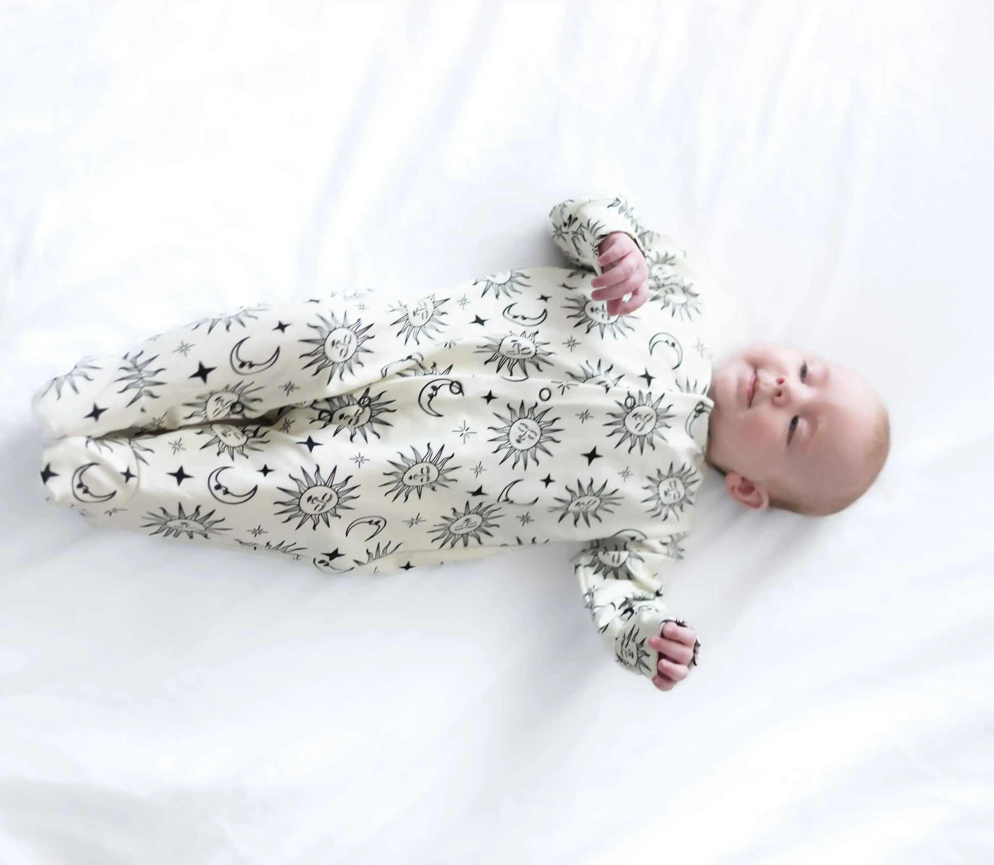 Baby wearing a white sleepsuit with black patterns on a white background