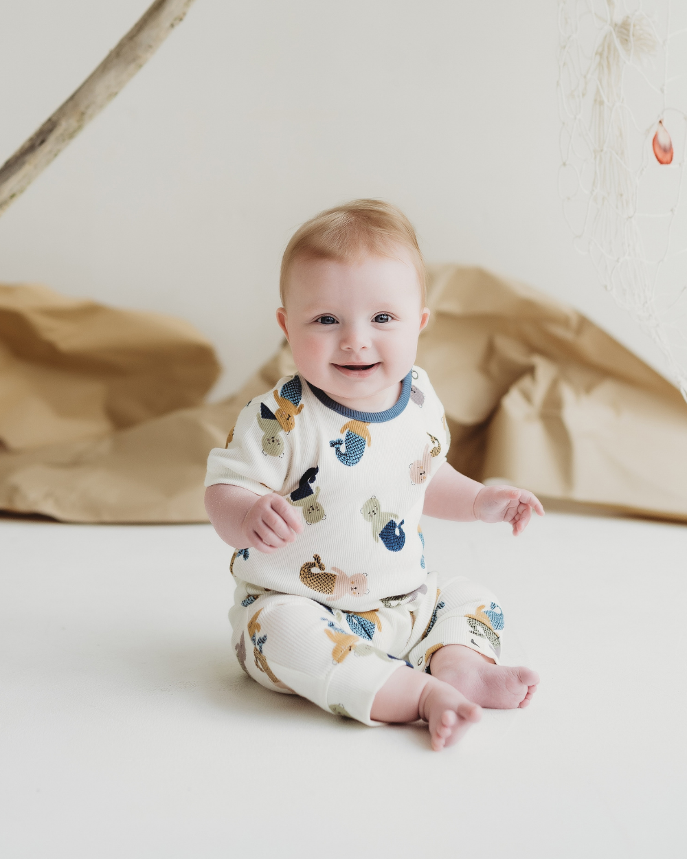 Baby wearing a sleepsuit with animal prints sitting on a white surface.