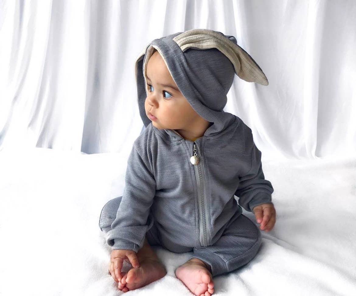 Baby wearing a gray sleepsuit with bunny ears on a white background