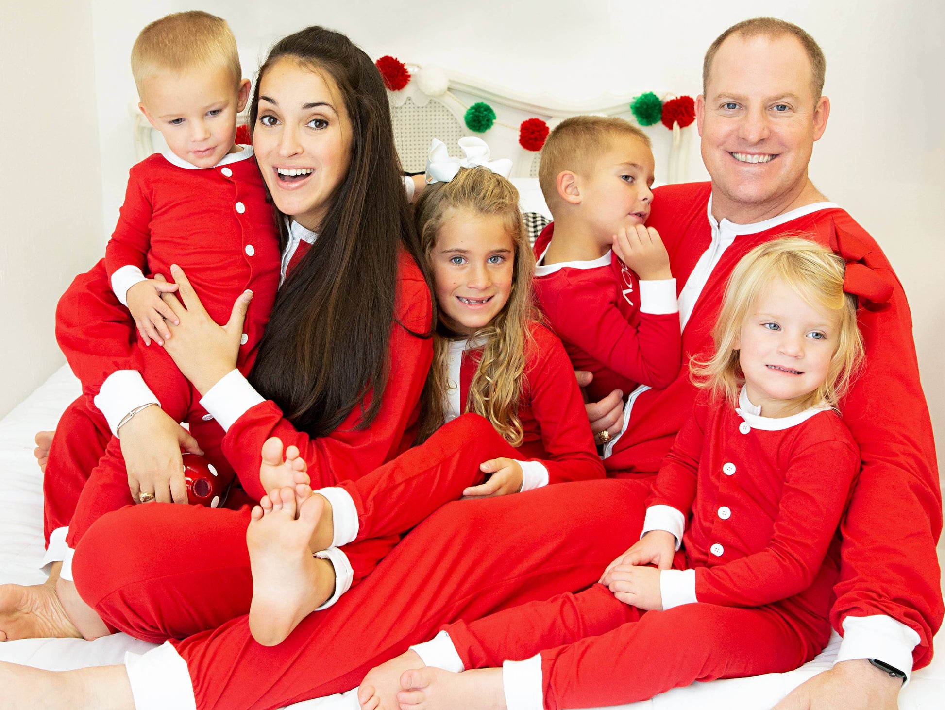 Family in matching red pajamas posing together on a white background