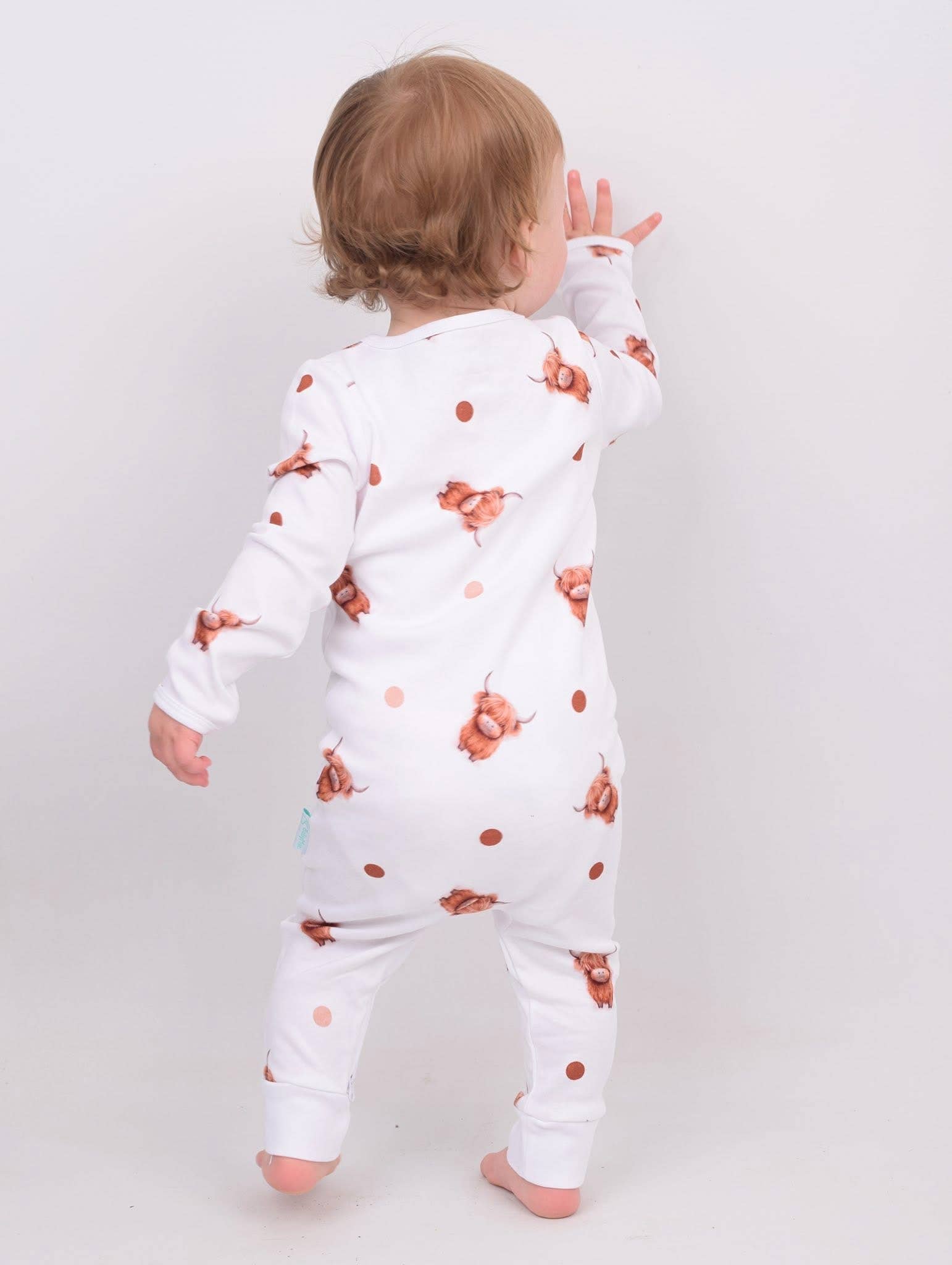 Baby wearing a white sleepsuit with orange floral patterns on a plain background