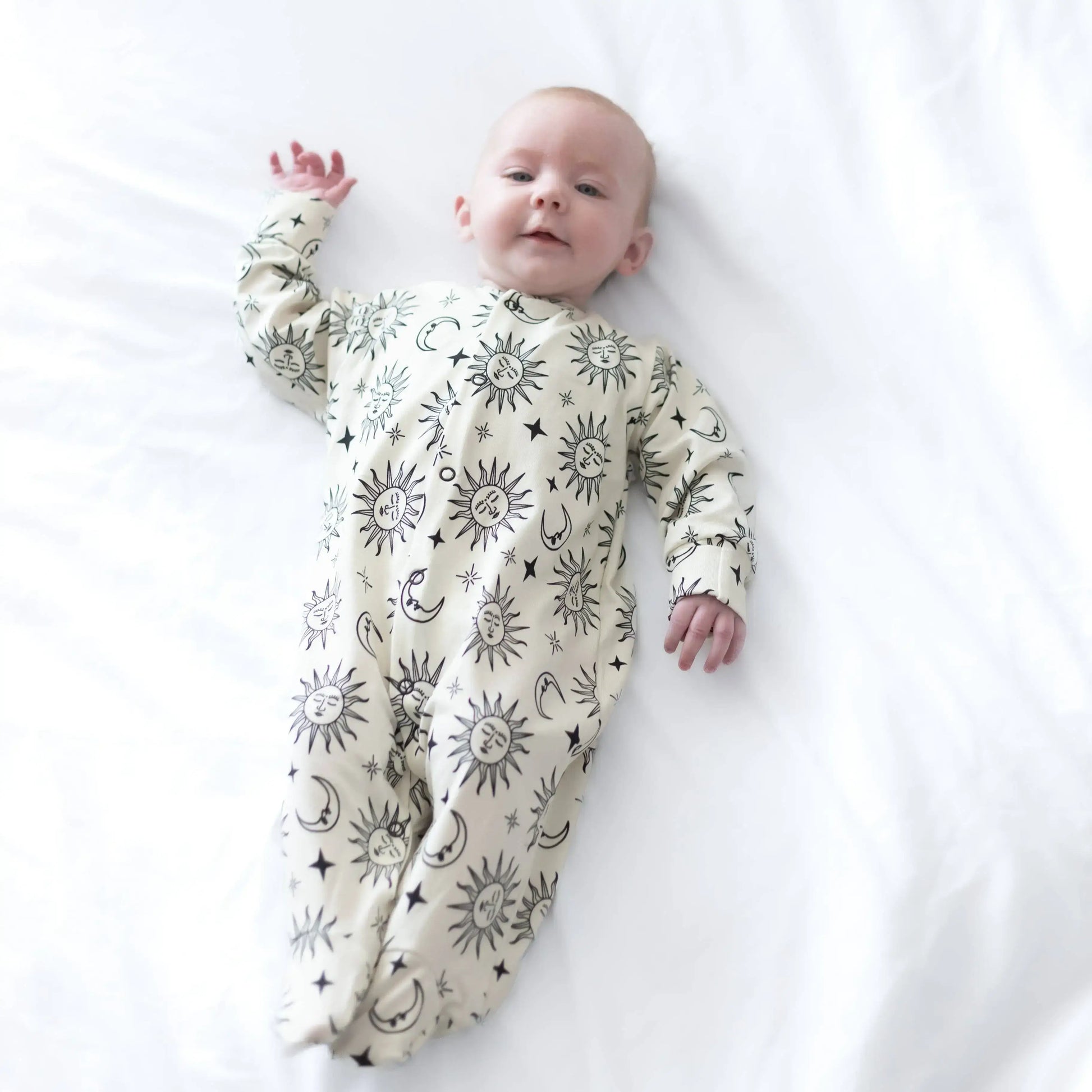 Baby lying on a white surface wearing a sleepsuit with celestial pattern