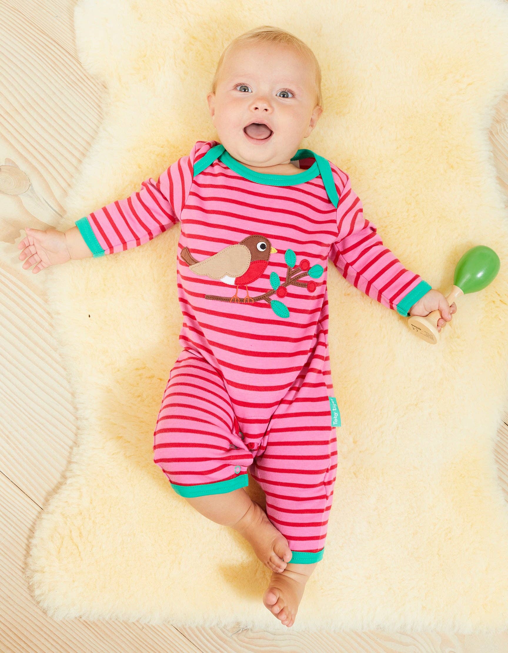 Baby in a pink and green striped outfit lying on a yellow blanket