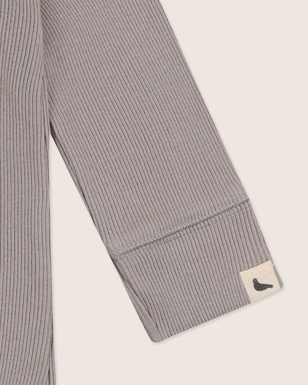 Gray ribbed bodysuit sleeve with a brand label on a light beige background
