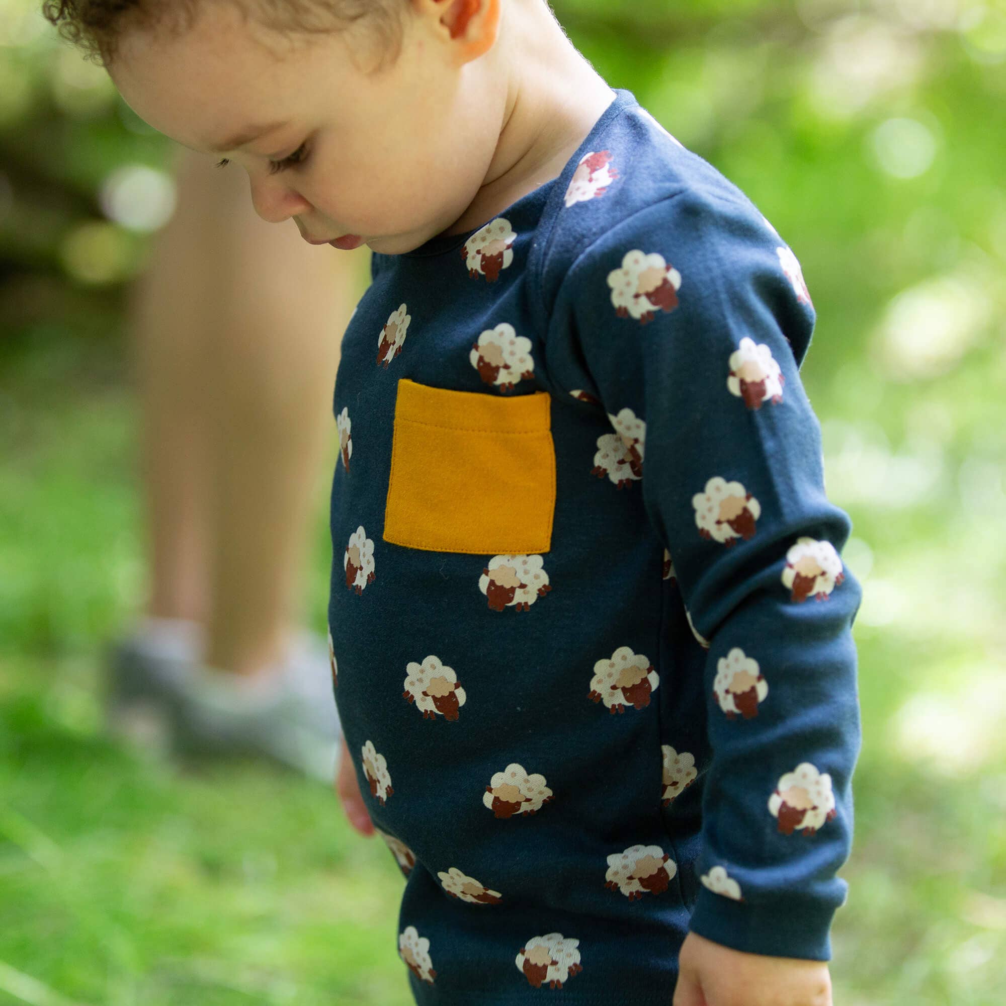 Child wearing a blue sweater with cloud patterns and a yellow pocket outdoors.