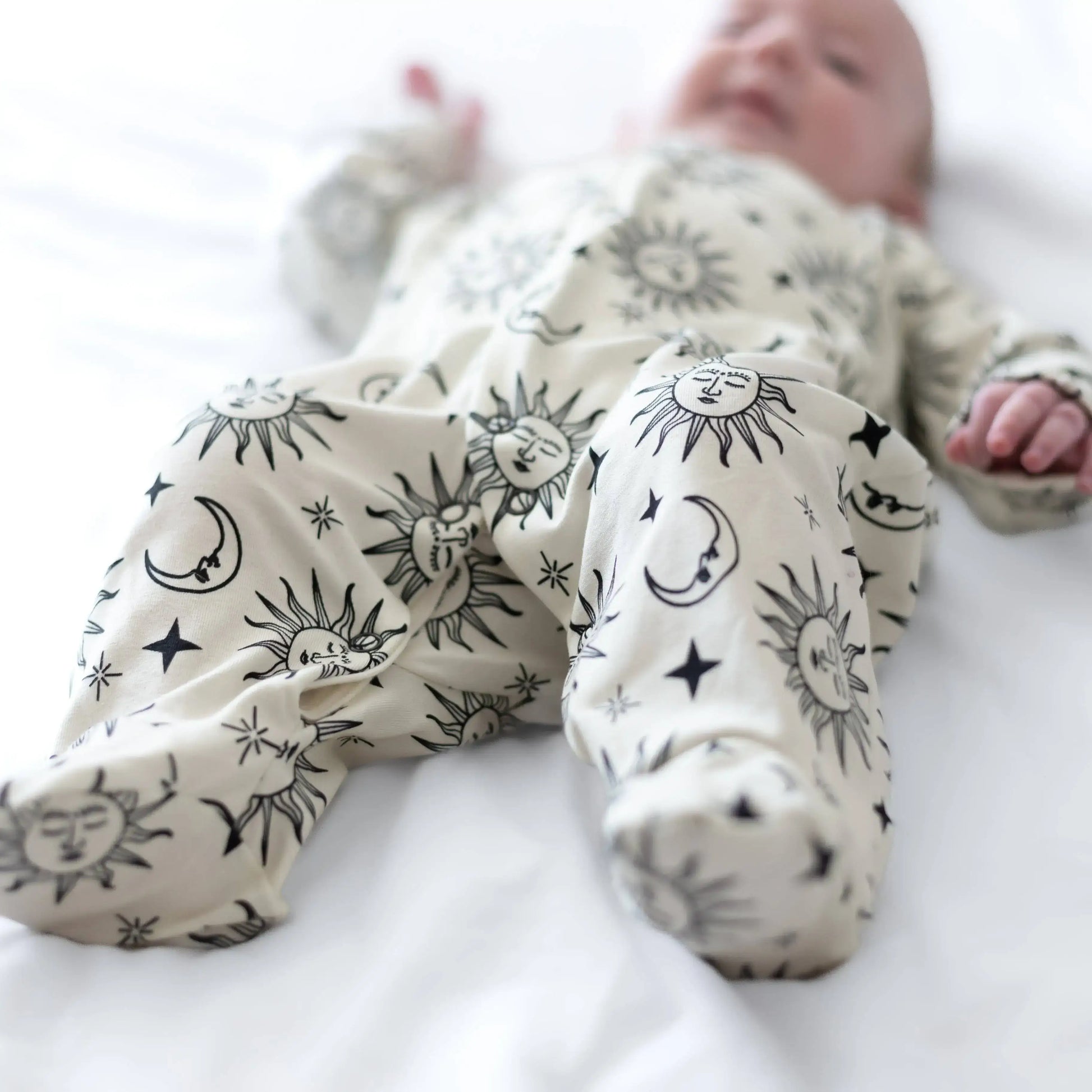 Baby wearing a white sleepsuit with black celestial patterns on a white background