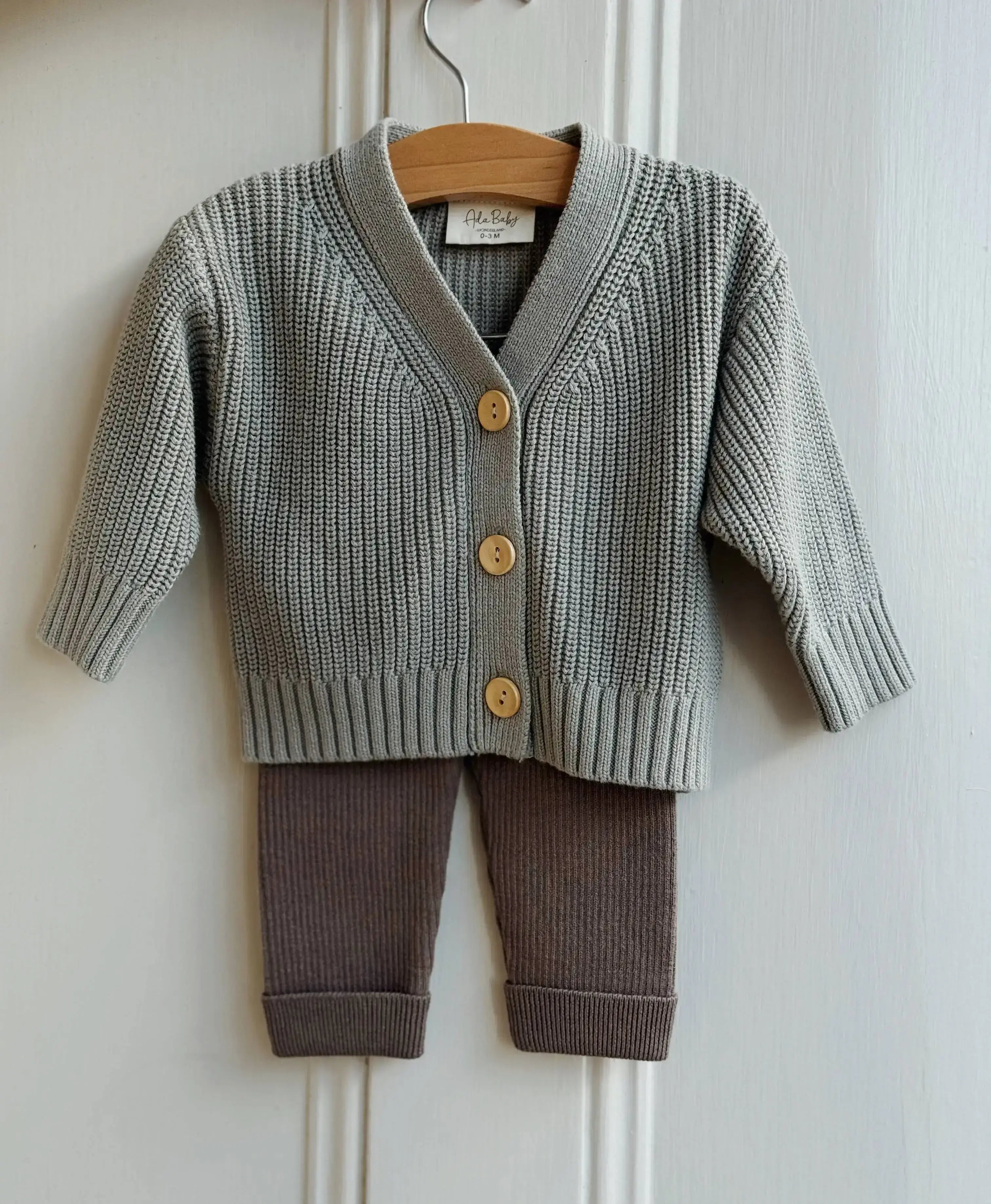 Baby sweater and pants set on a hanger against a white wall