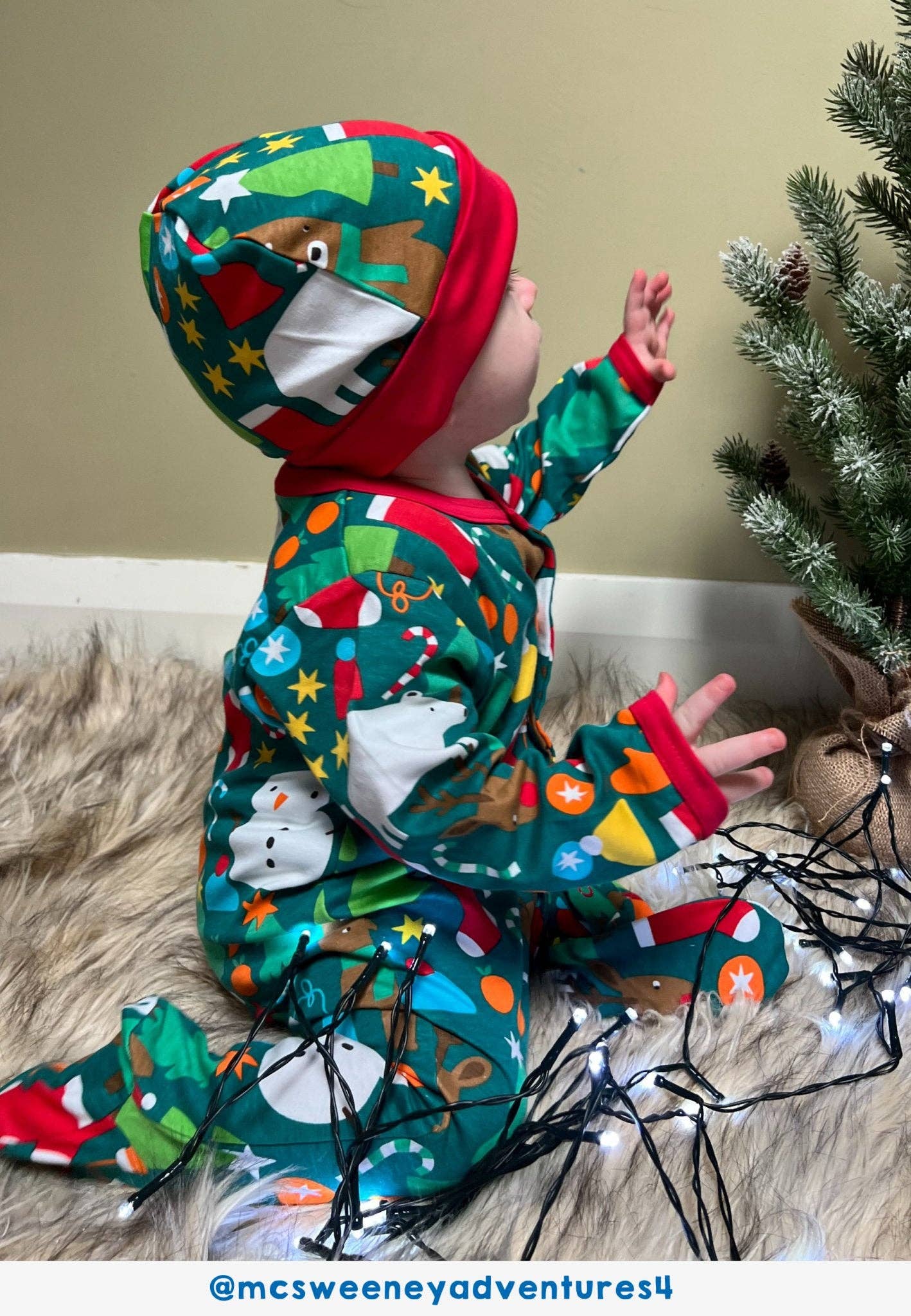 Child in festive pajamas with a Christmas tree and lights in the background