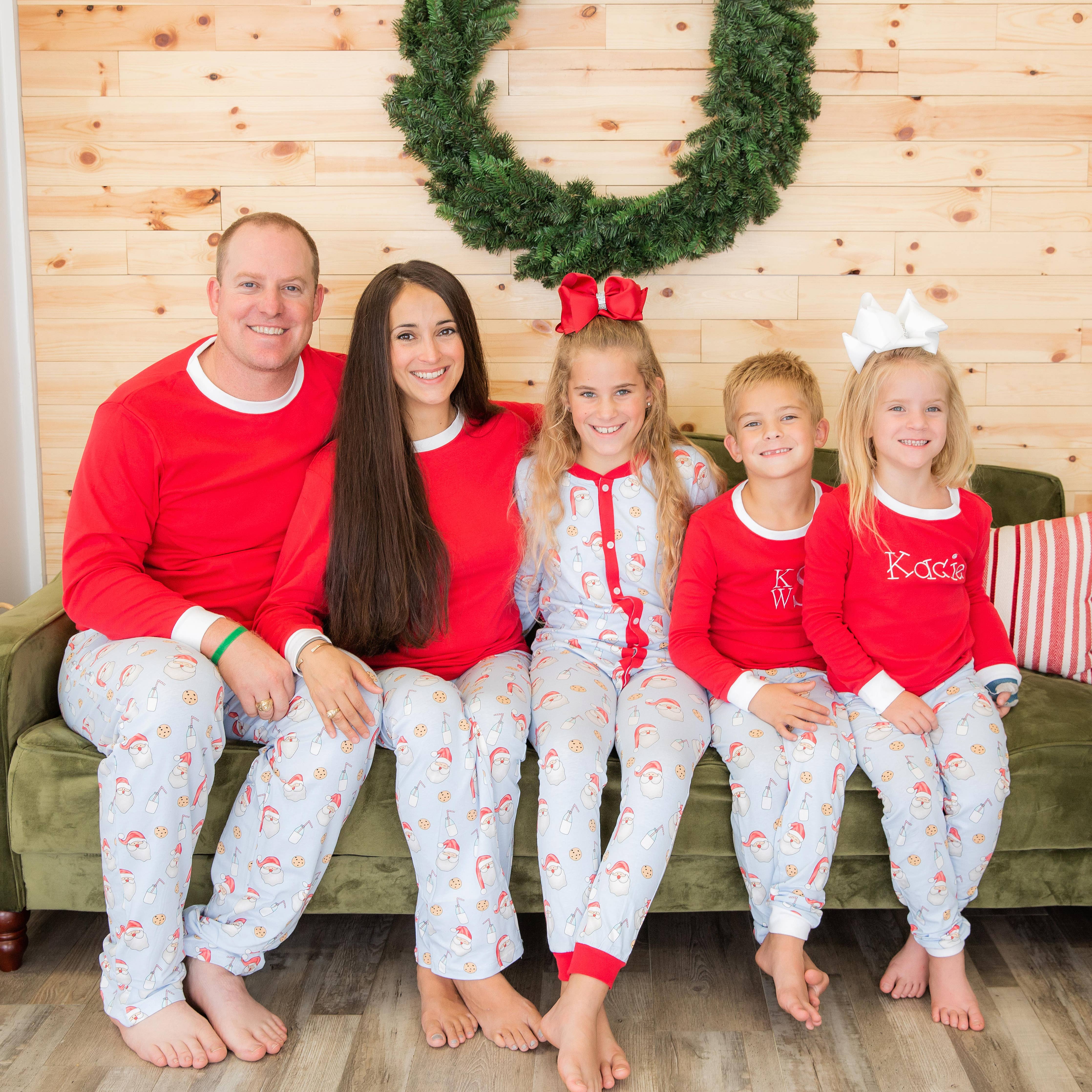 Family of five wearing matching red and white pajamas sitting on a couch with a Christmas wreath in the background.