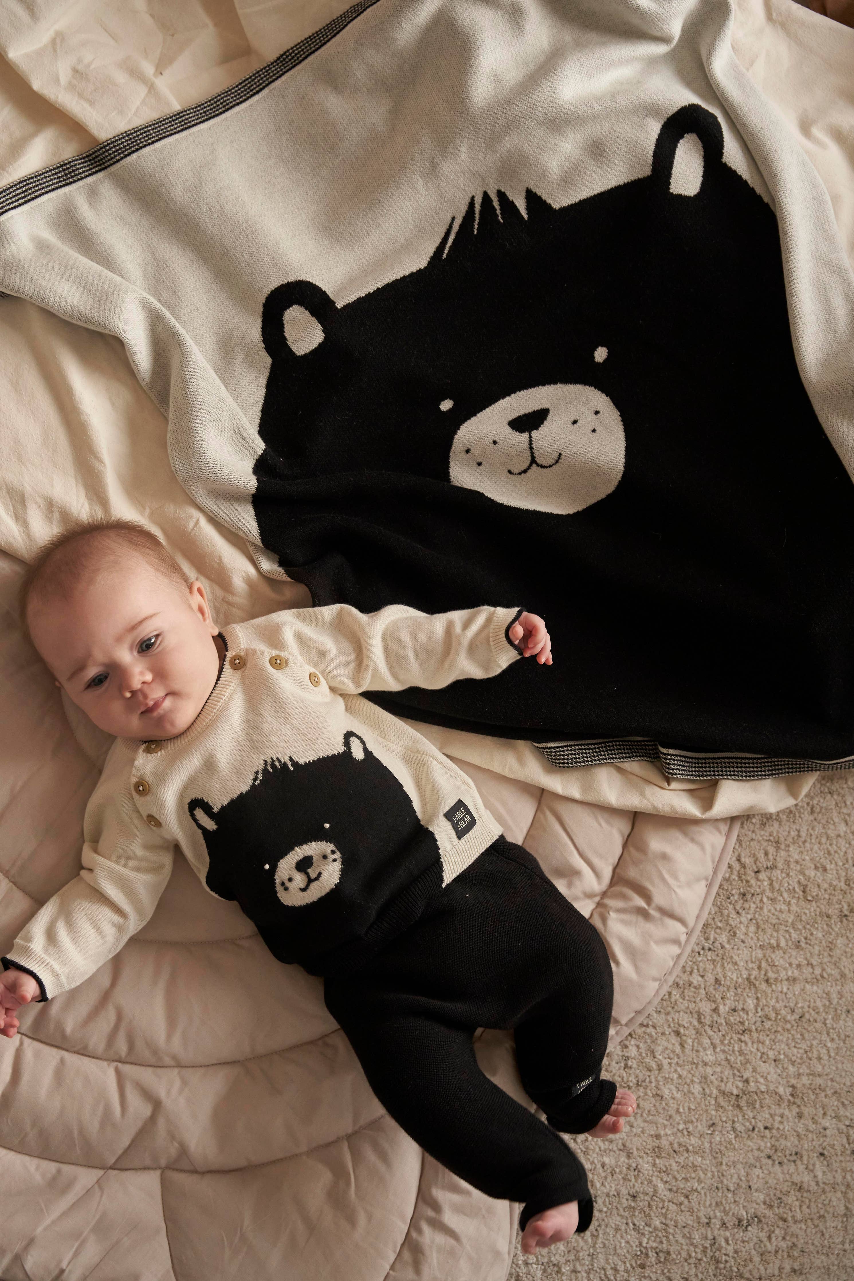 Baby lying on a bed with a black bear-shaped blanket