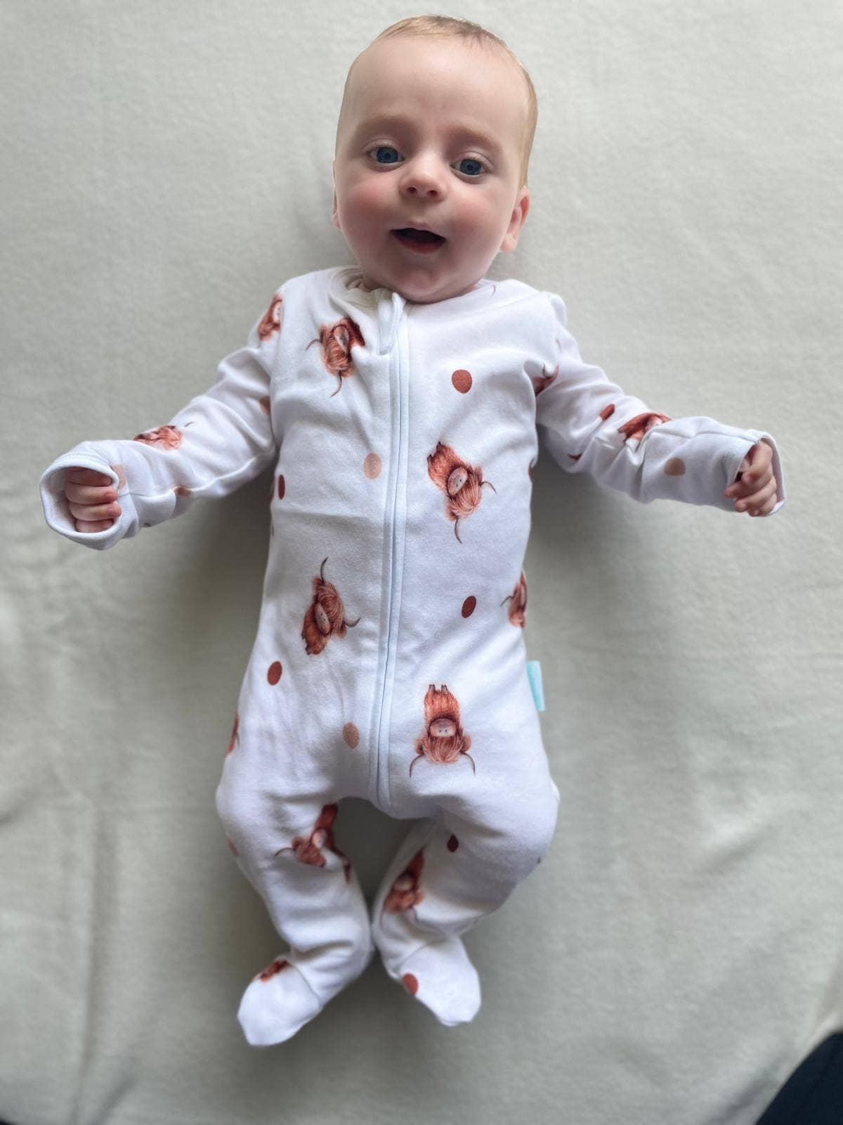 Baby wearing a white sleepsuit with orange fox patterns on a light gray background