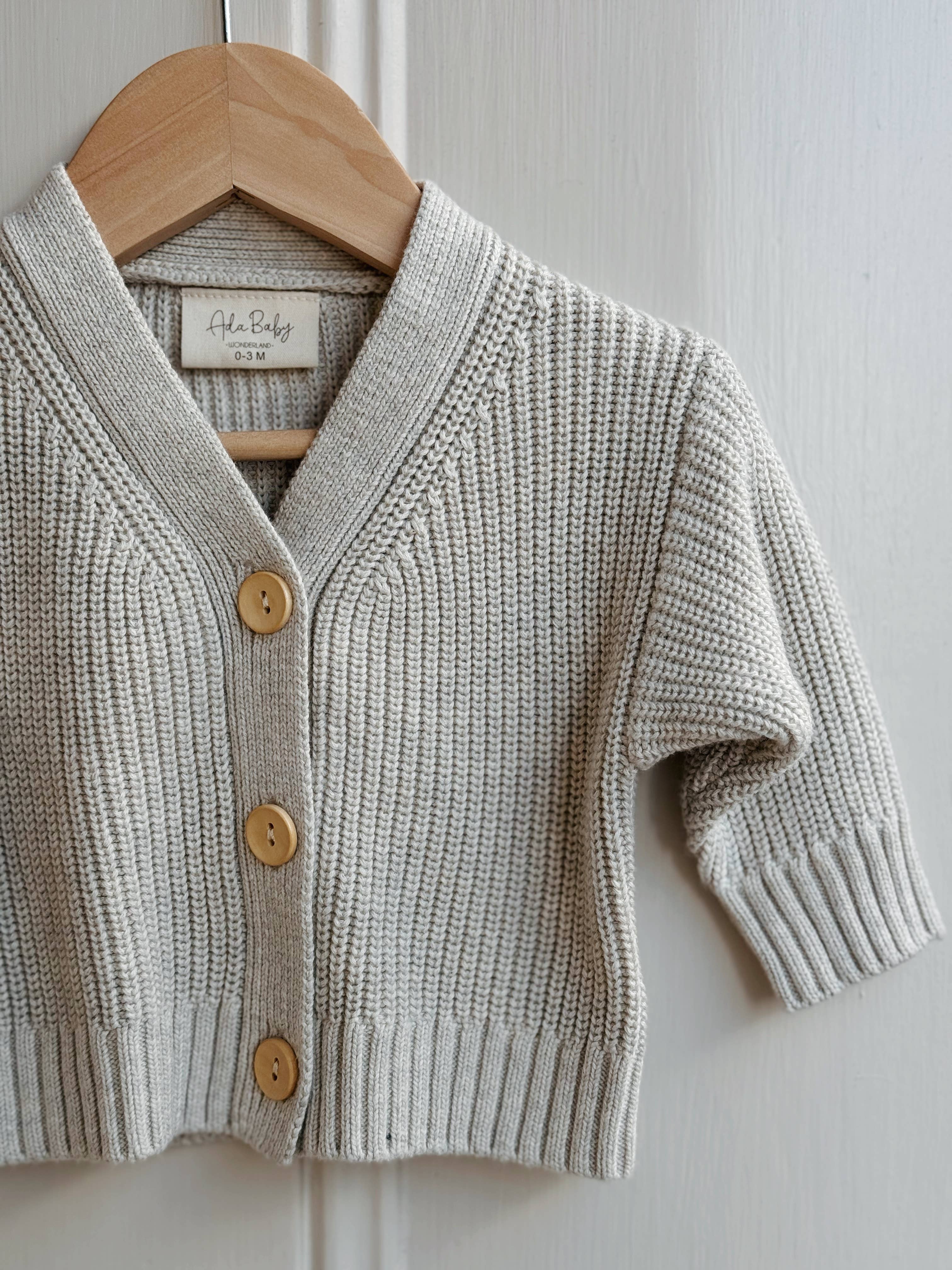 Melange knitted cardigan with wooden buttons on a hanger against a white background