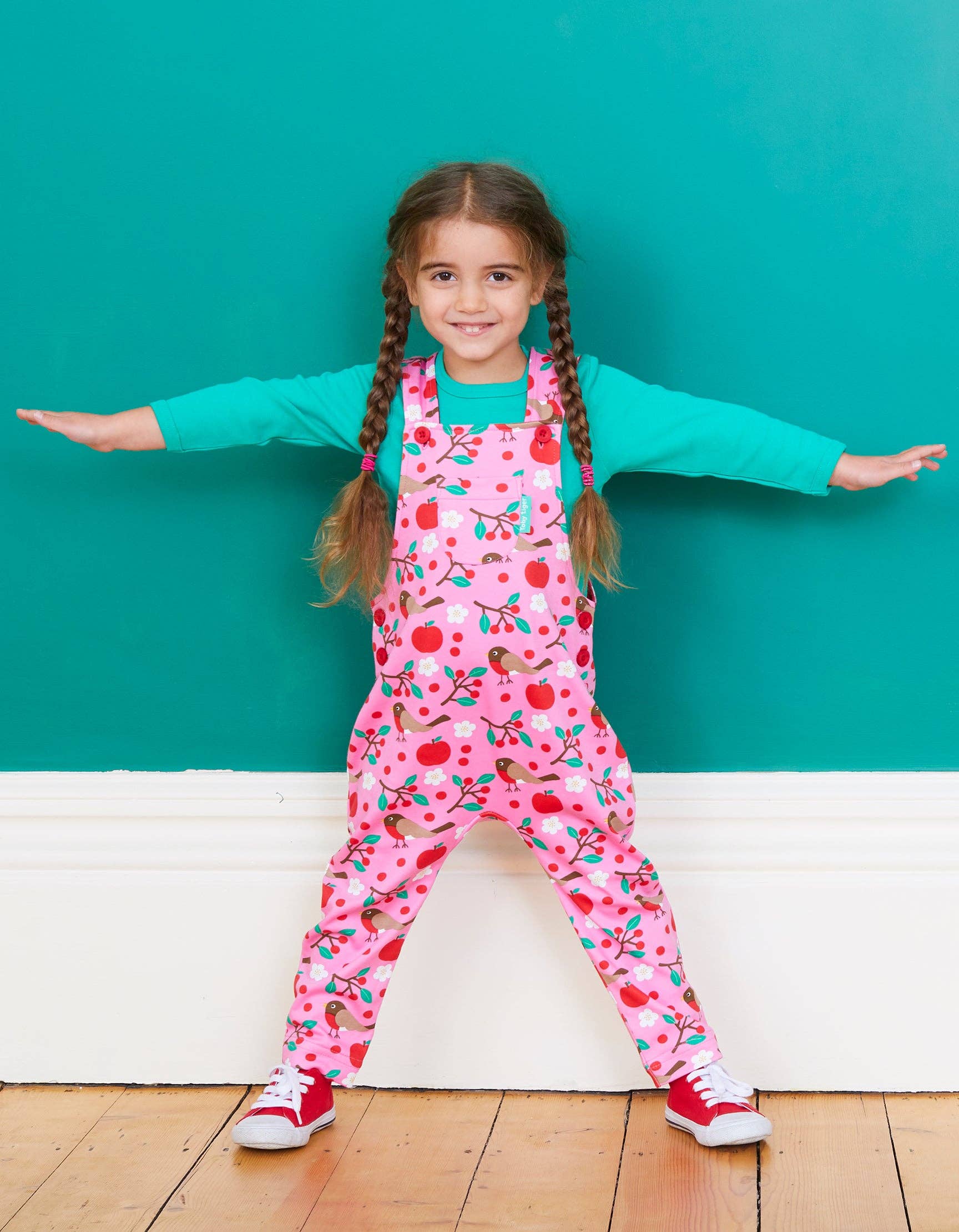 Young girl wearing a pink floral jumpsuit with a teal background