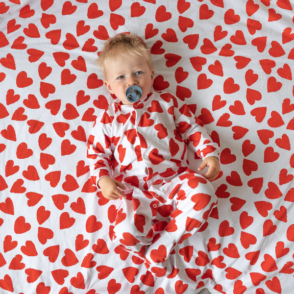 Baby lying on a white blanket with red heart patterns