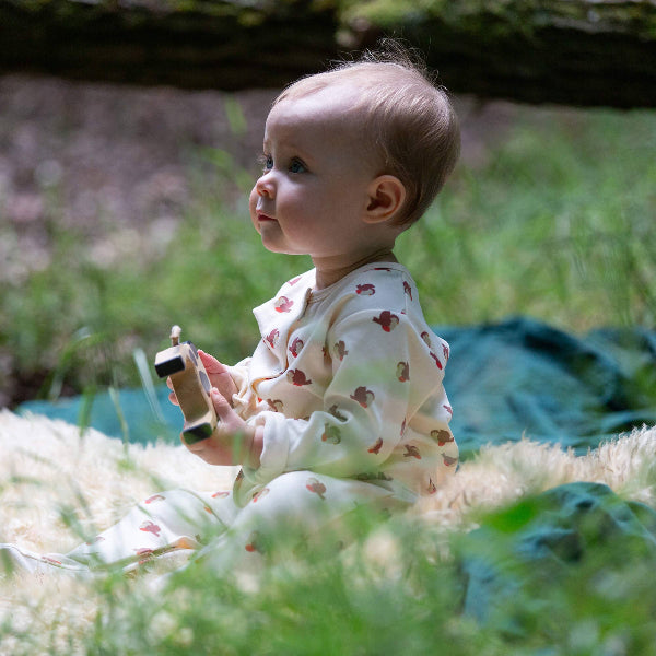 Baby sitting on a blanket in a grassy area holding a wooden toy.