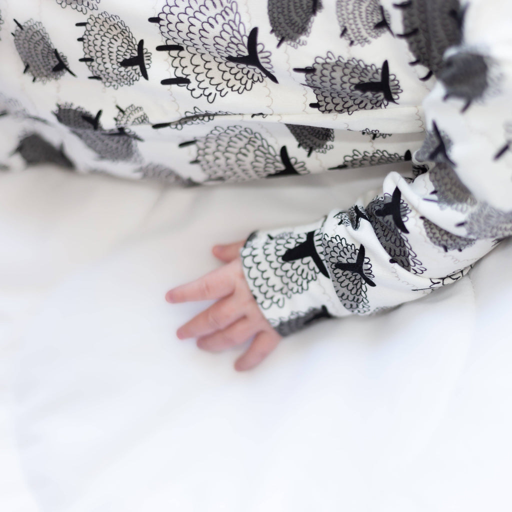Baby's hand wearing a sleeve with sheep pattern on a white background