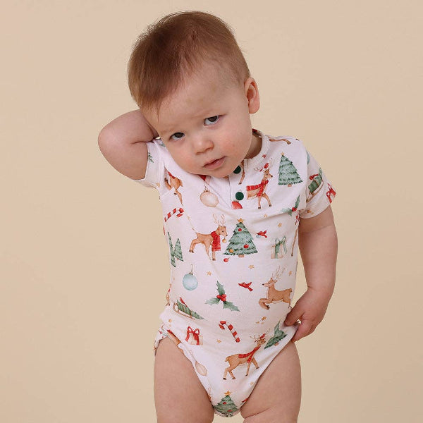 Baby wearing a onesie with Christmas-themed designs on a beige background