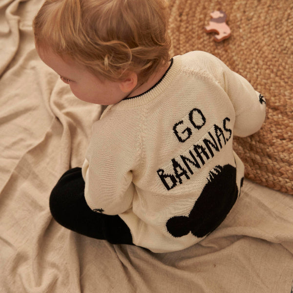 Child wearing a jumper/sweater with 'GO BANANAS' text sitting on a beige blanket.