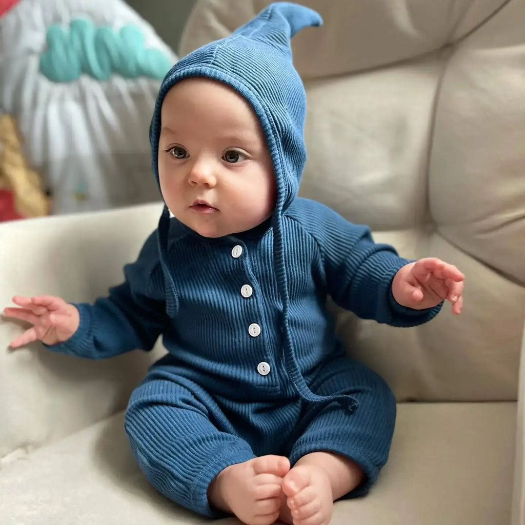 Baby wearing a blue romper with a matching hat on a beige couch.