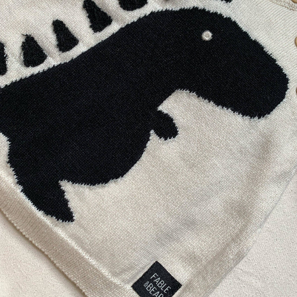 Close-up of a baby blanket with a black dinosaur silhouette on a light gray background, featuring the brand 'Fable & Bear'.