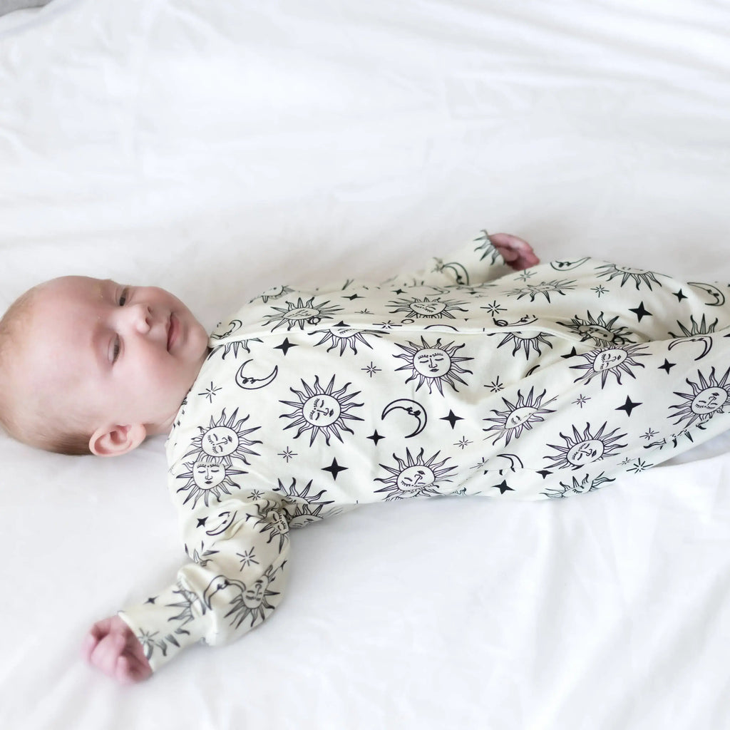 Baby wearing sleepsuit with celestial patterns on a white background