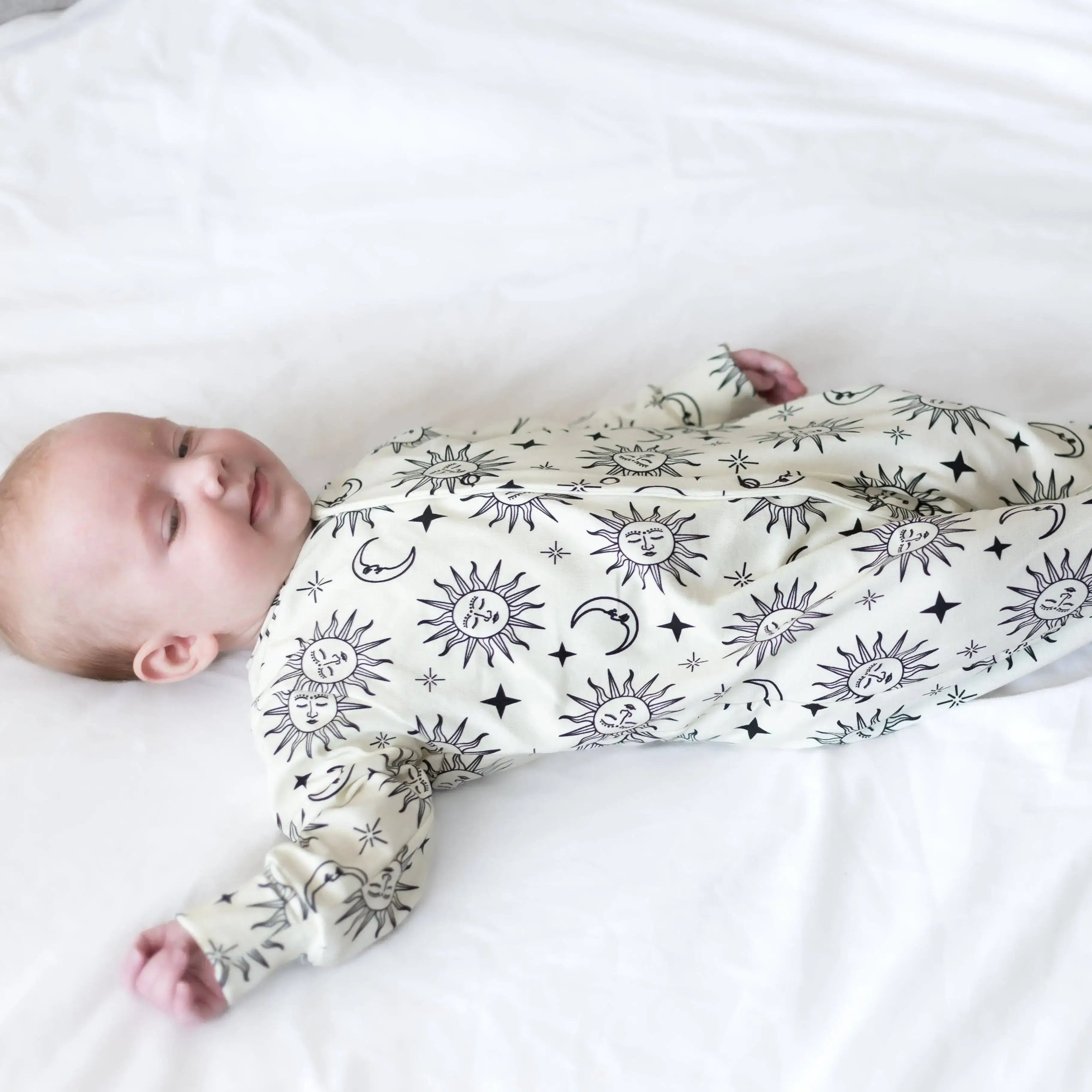 Baby wearing sleepsuit with celestial patterns on a white background