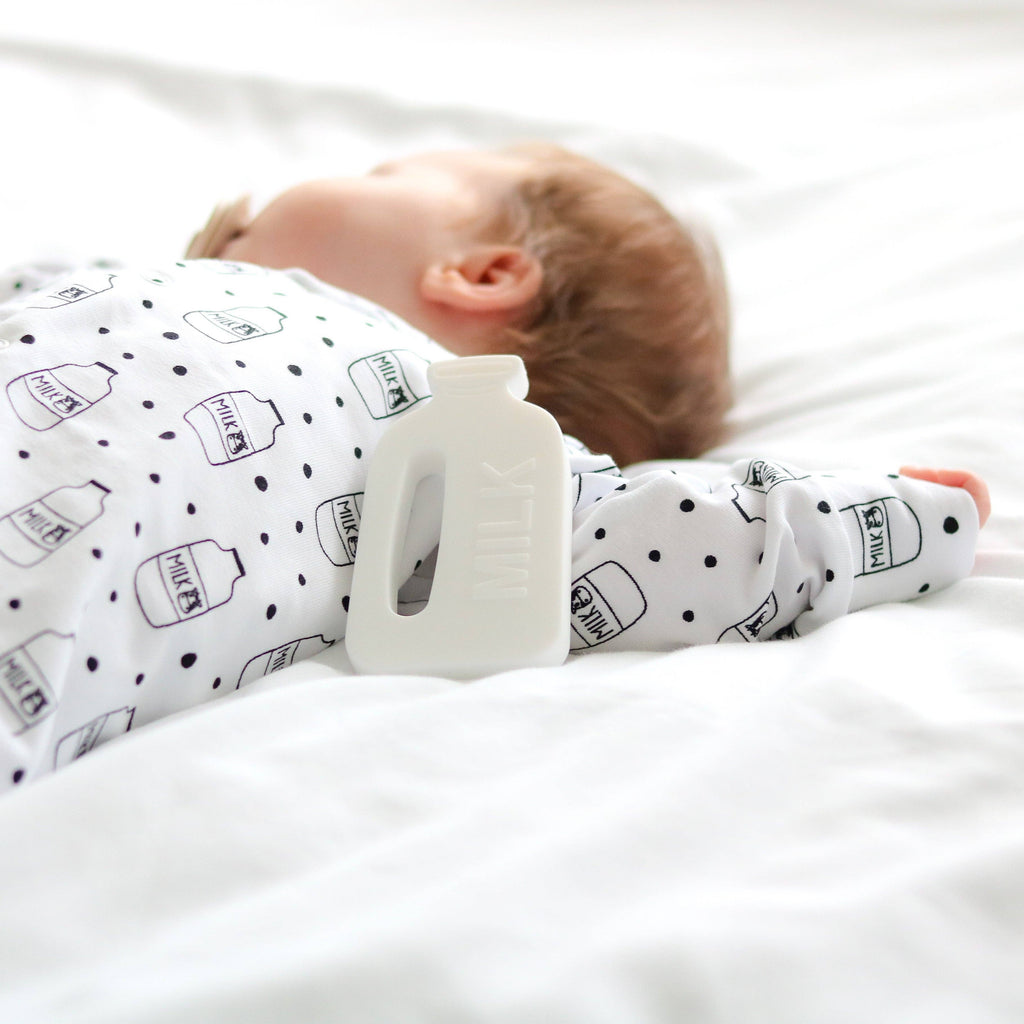 Baby lying on a white surface wearing a sleepsuit with bottle patterns.