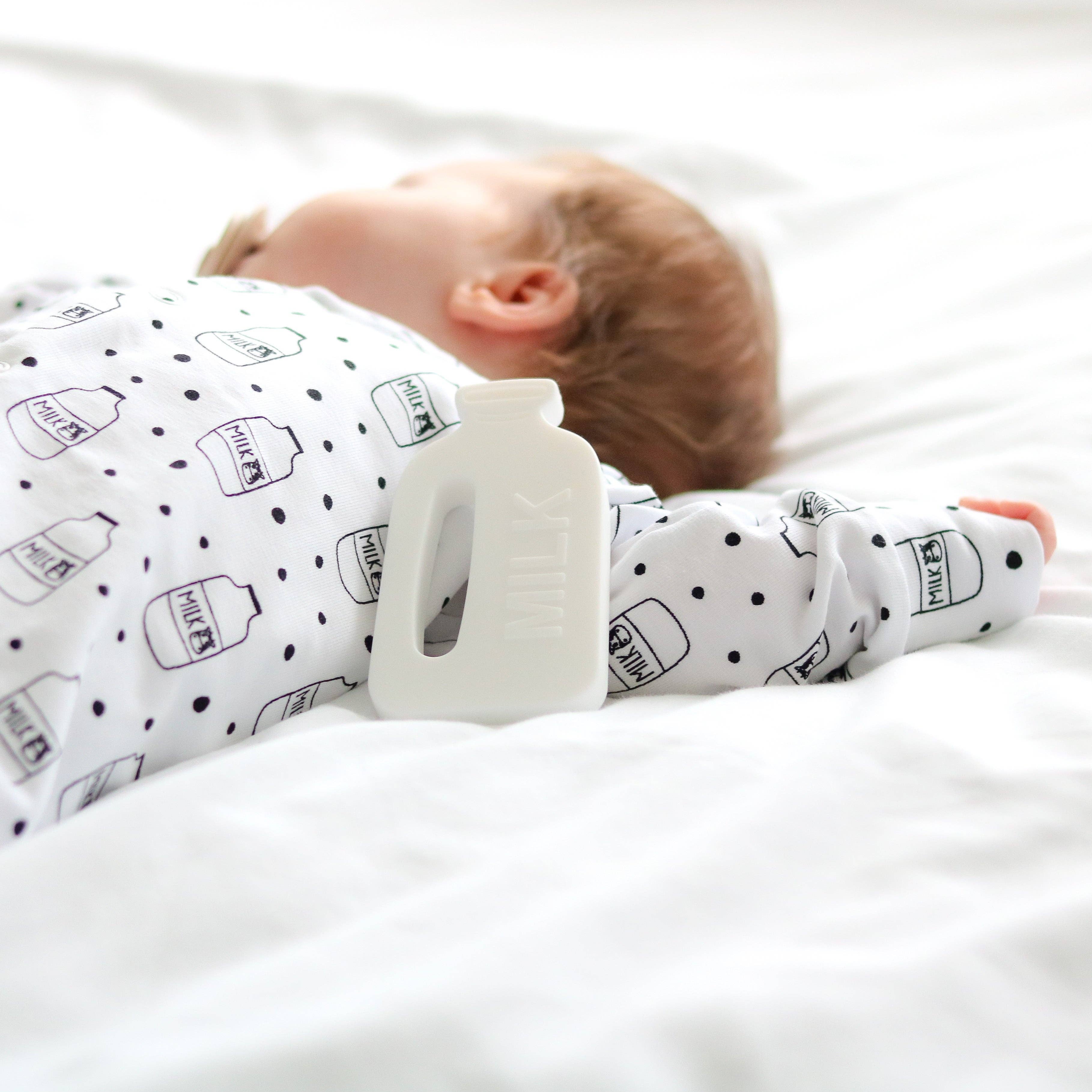 Baby lying on a white surface wearing a sleepsuit with bottle patterns.