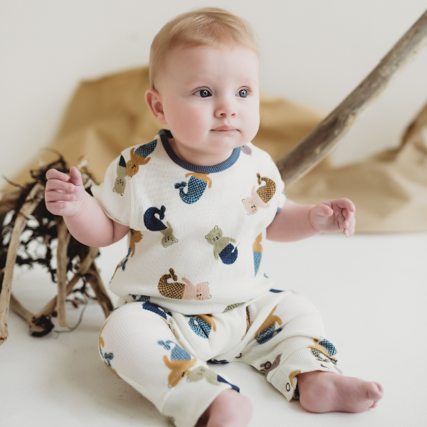 Baby wearing a sleepsuit with animal prints sitting on a white surface.