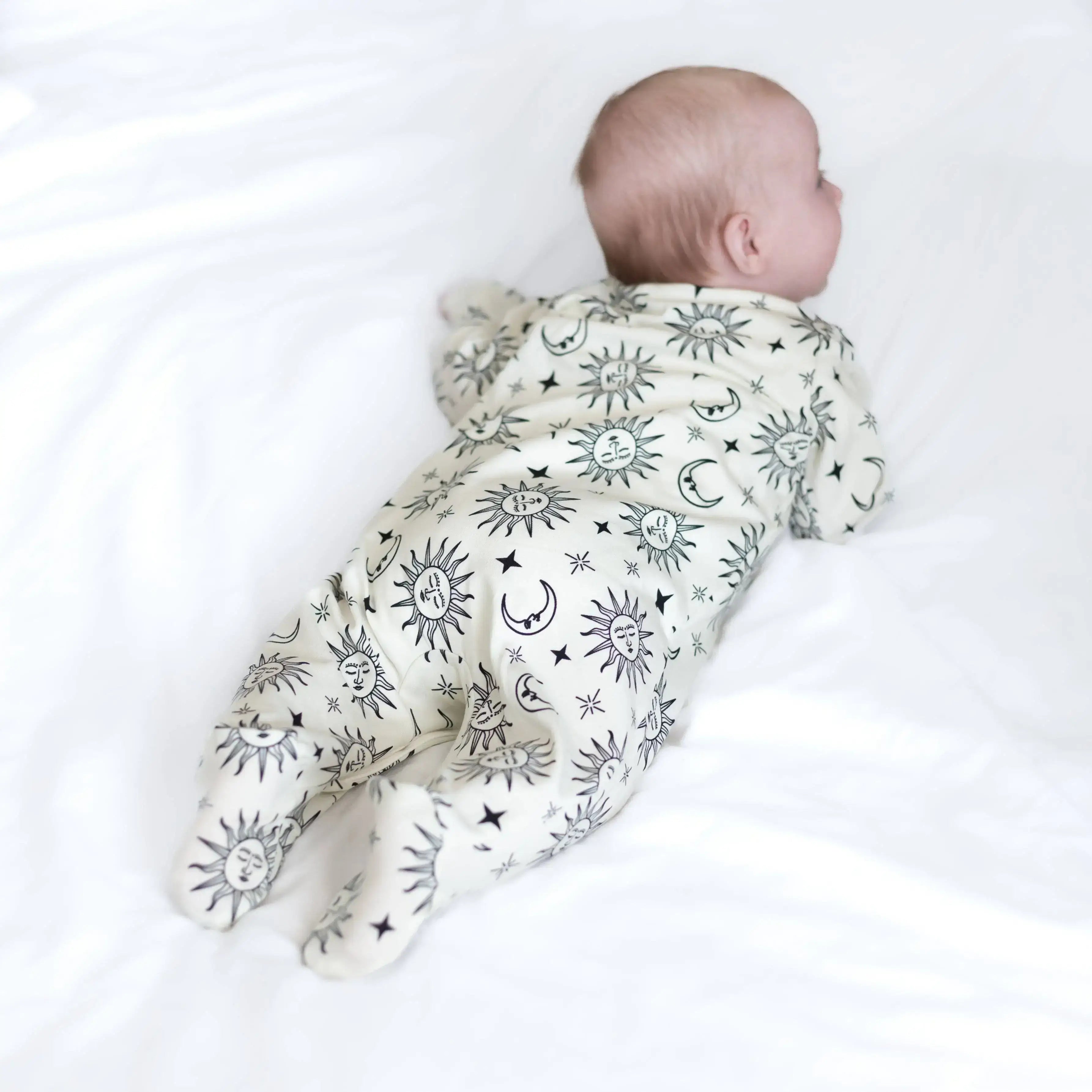 Baby wearing sleepsuit with celestial pattern on a white background