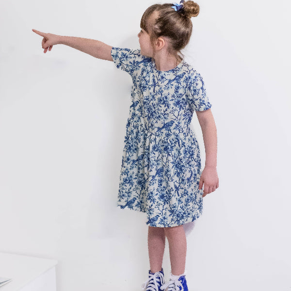 Child wearing a blue floral dress pointing to the side on a white background