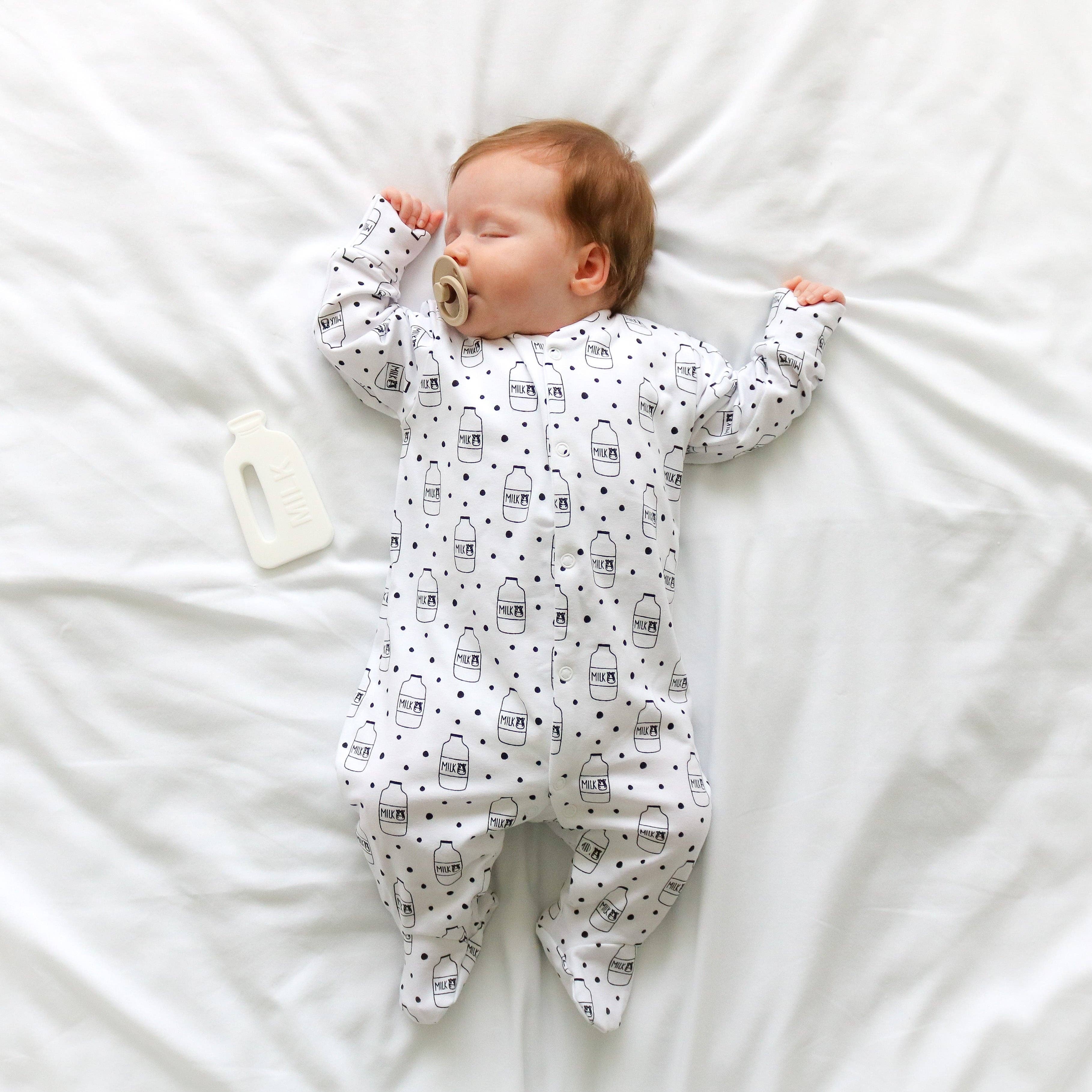 Baby lying on a white blanket wearing a sleepsuit with black patterns