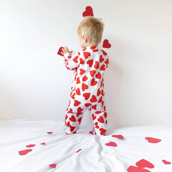 Child wearing a red heart-patterned onesie on a white background with scattered hearts.
