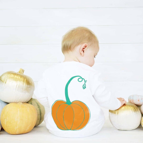 Baby wearing a sleepsuit with a pumpkin design, surrounded by decorative pumpkins on a white background