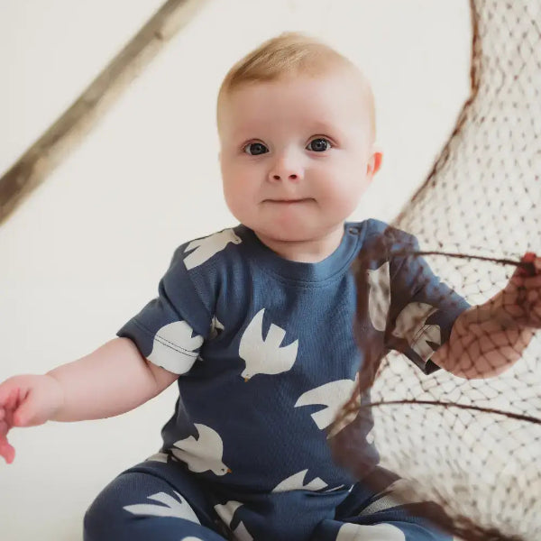 Baby wearing a navy blue outfit with white bird patterns, sitting on a wooden floor.