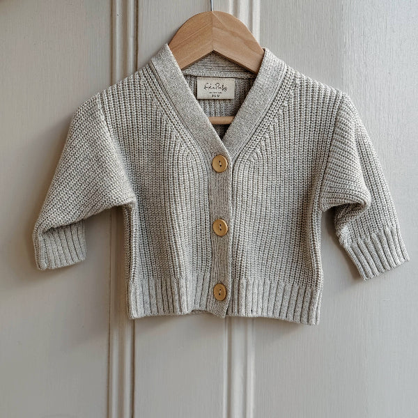 Baby cardigan with buttons on a wooden hanger against a white paneled wall