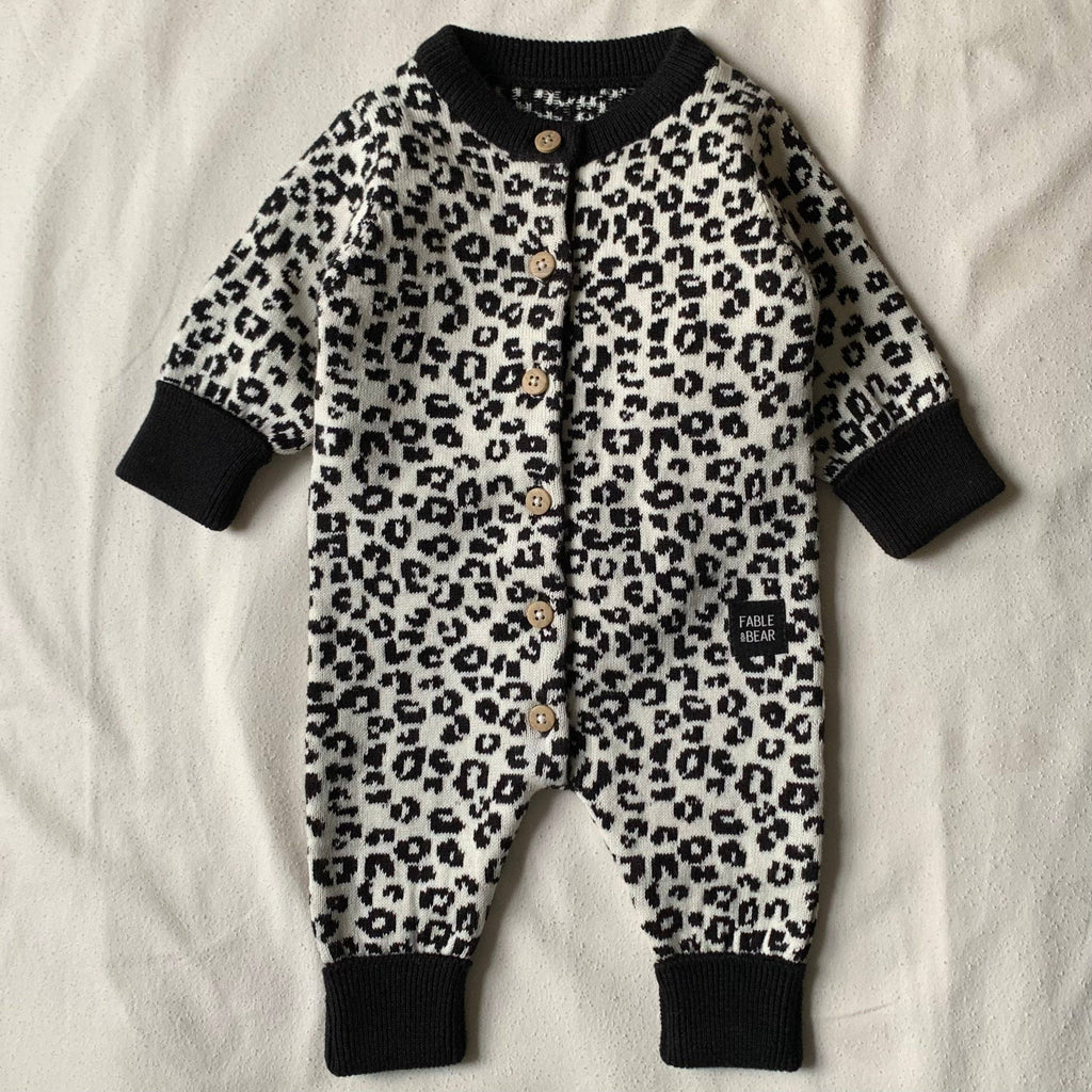 Leopard print baby romper with black cuffs and buttons on a light background