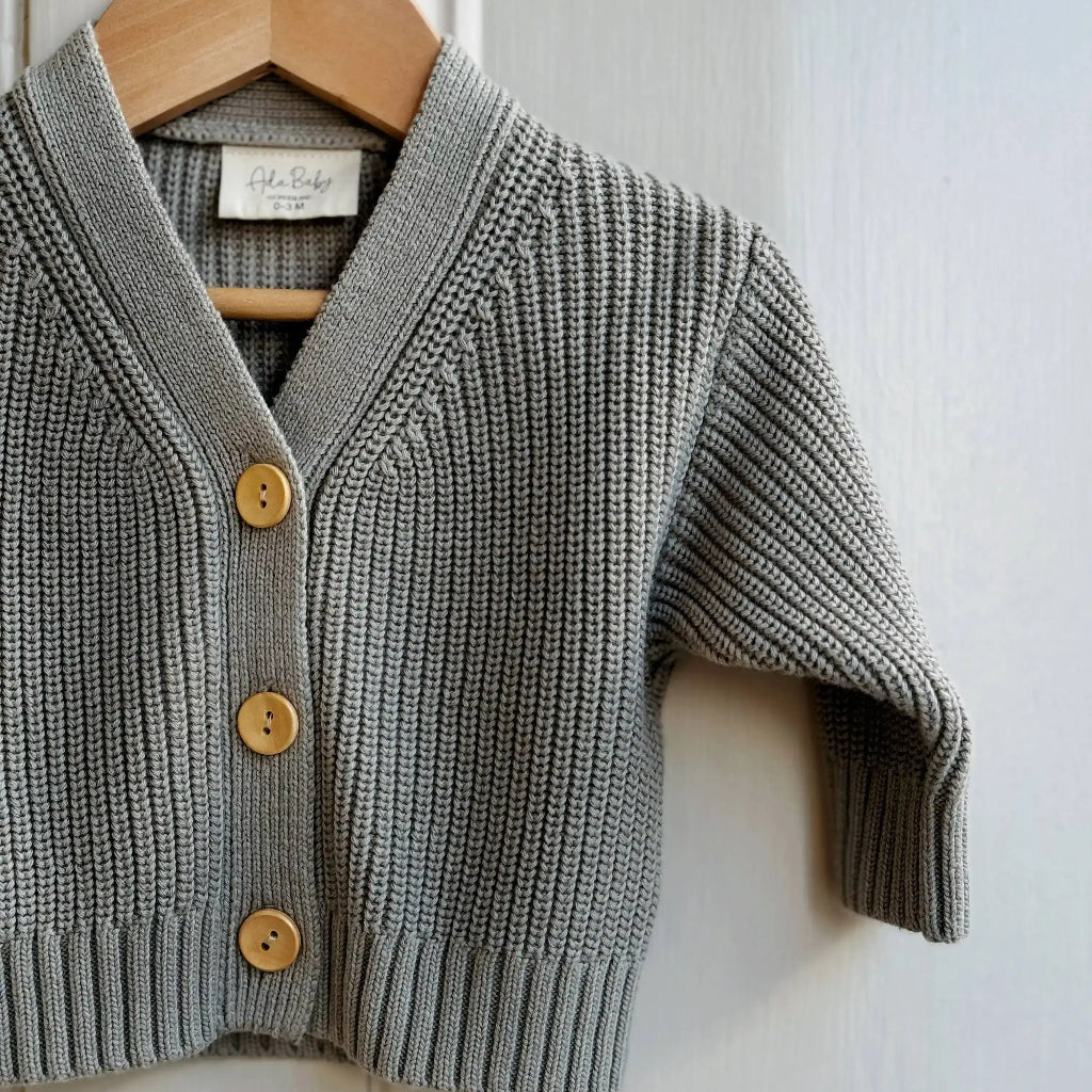 Light green knitted cardigan with wooden buttons on a hanger against a white background