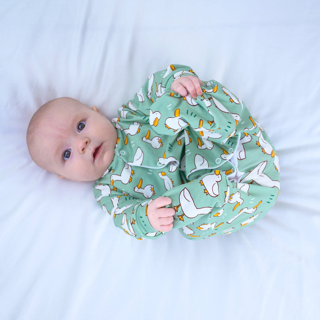 Baby wearing a green sleepsuit with animal pattern on a white background