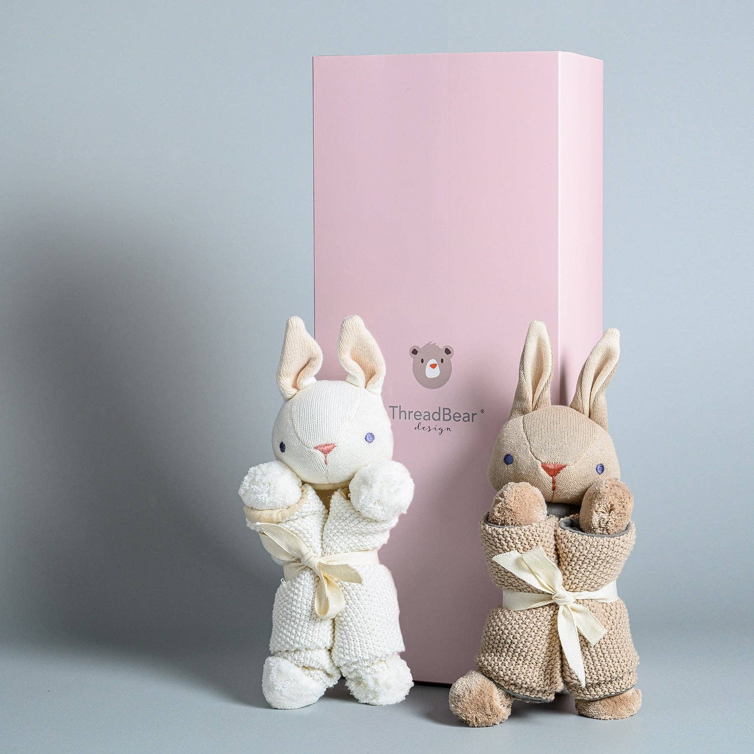 Two plush bunny toys wrapped in towels with a pink box in the background, featuring the ThreadBear Design logo.