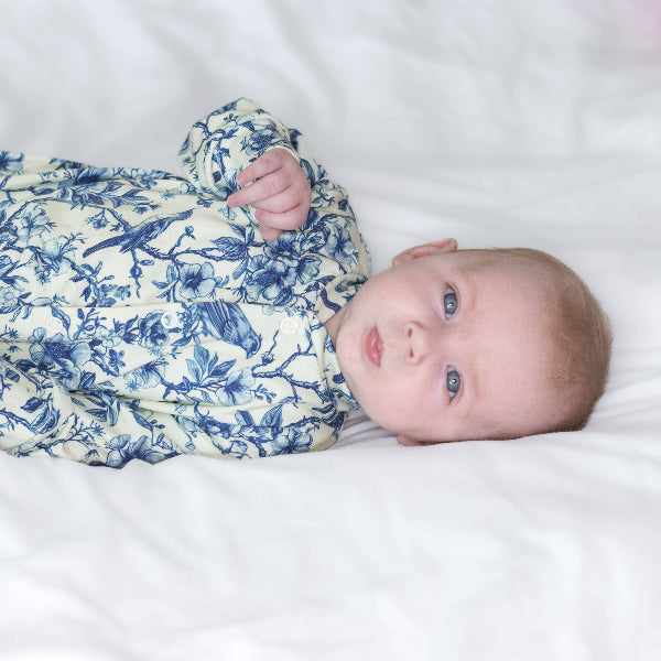 Baby wrapped in a blue and white floral swaddle on a white blanket