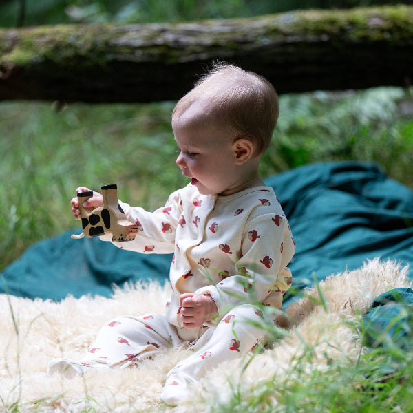 Baby sitting outdoors holding a toy, surrounded by greenery