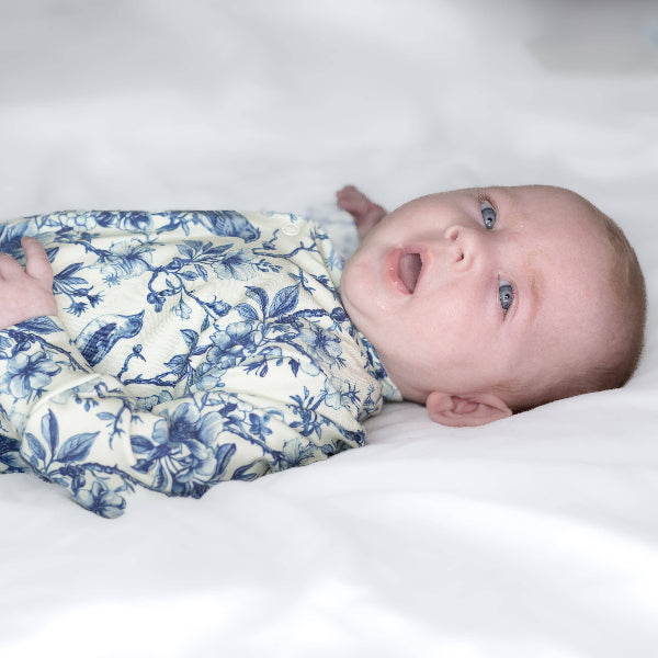 Baby wrapped in a blue floral blanket on a white surface