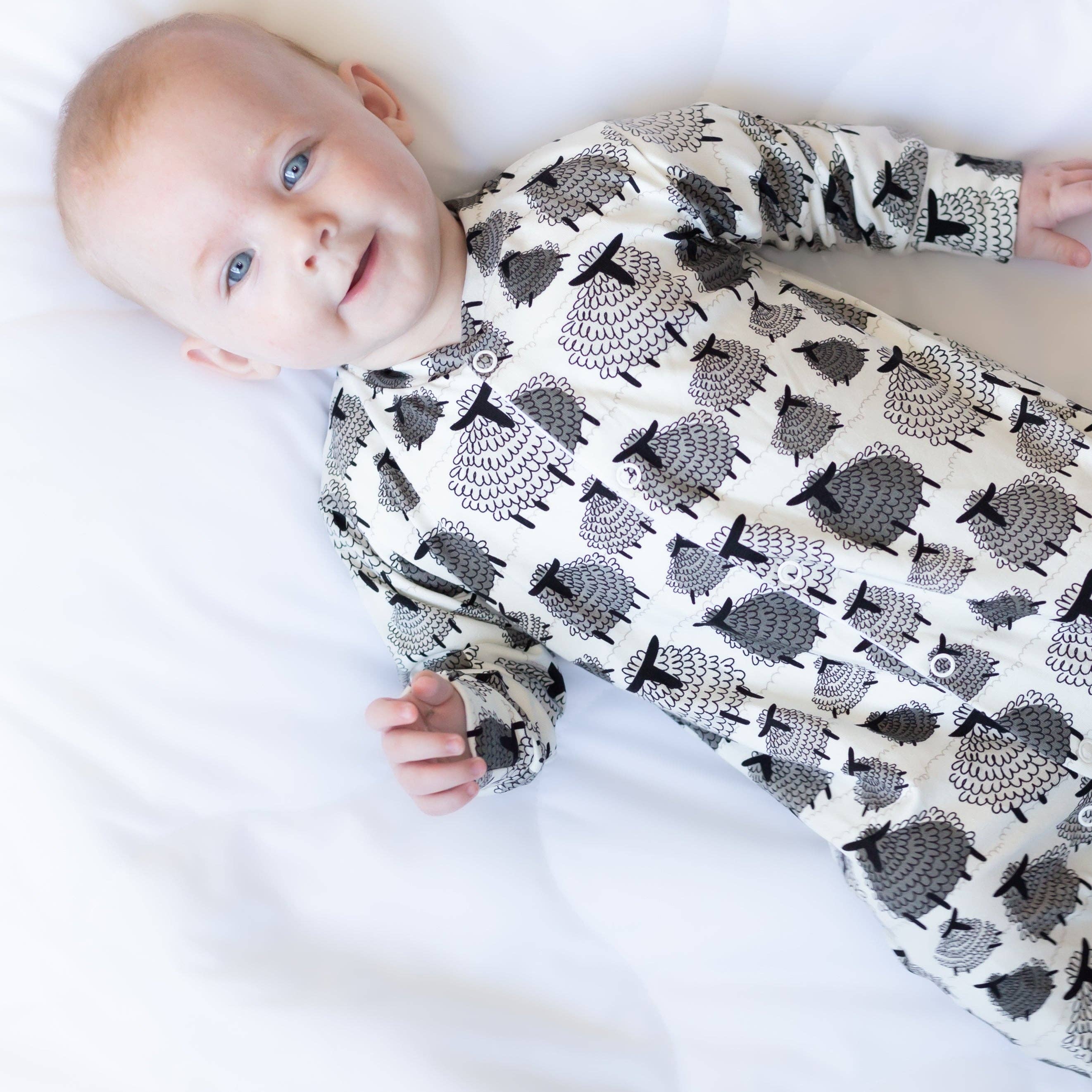 Baby wearing a sleepsuit with sheep pattern on a white background